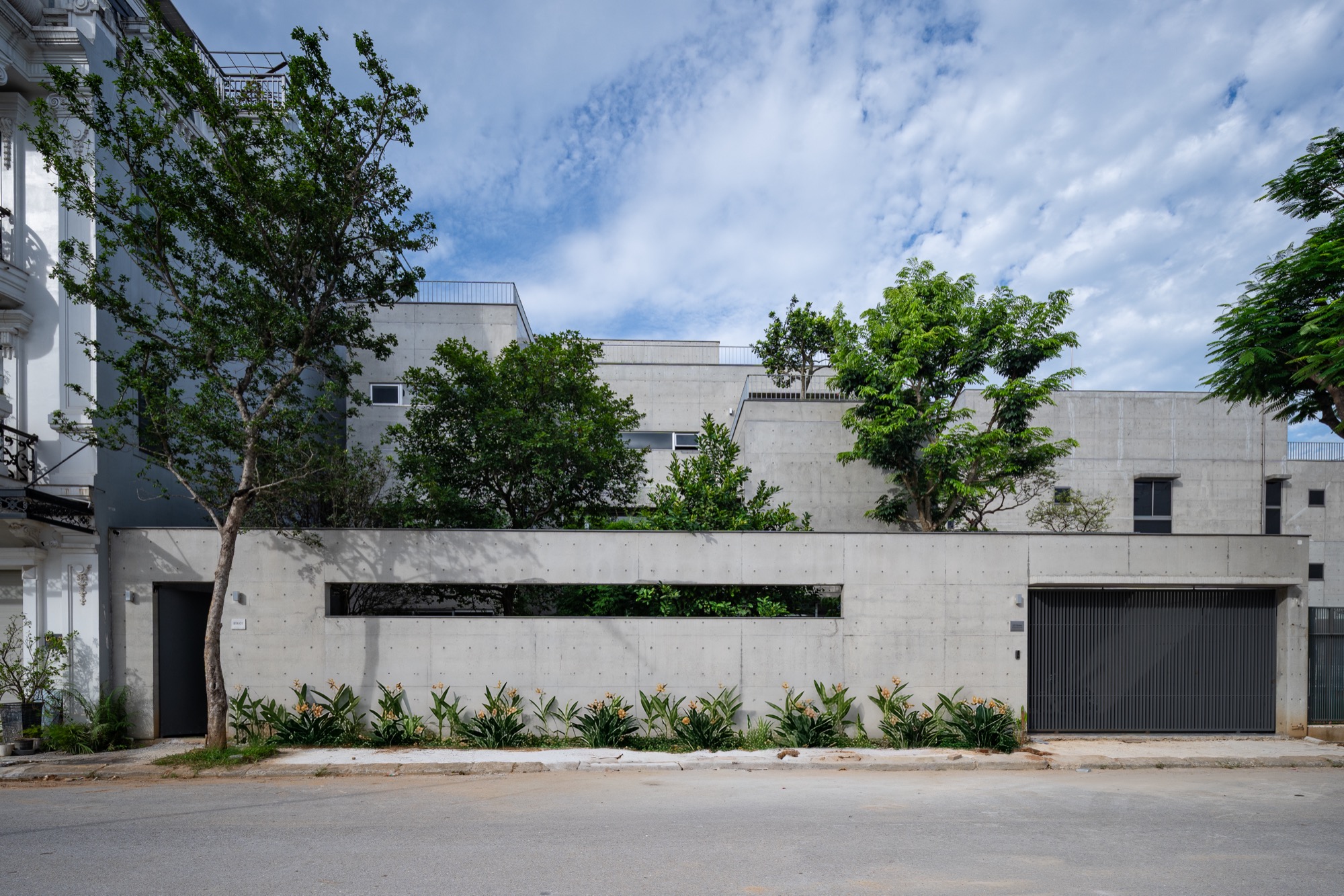Street view of the low concrete house behind its front garden