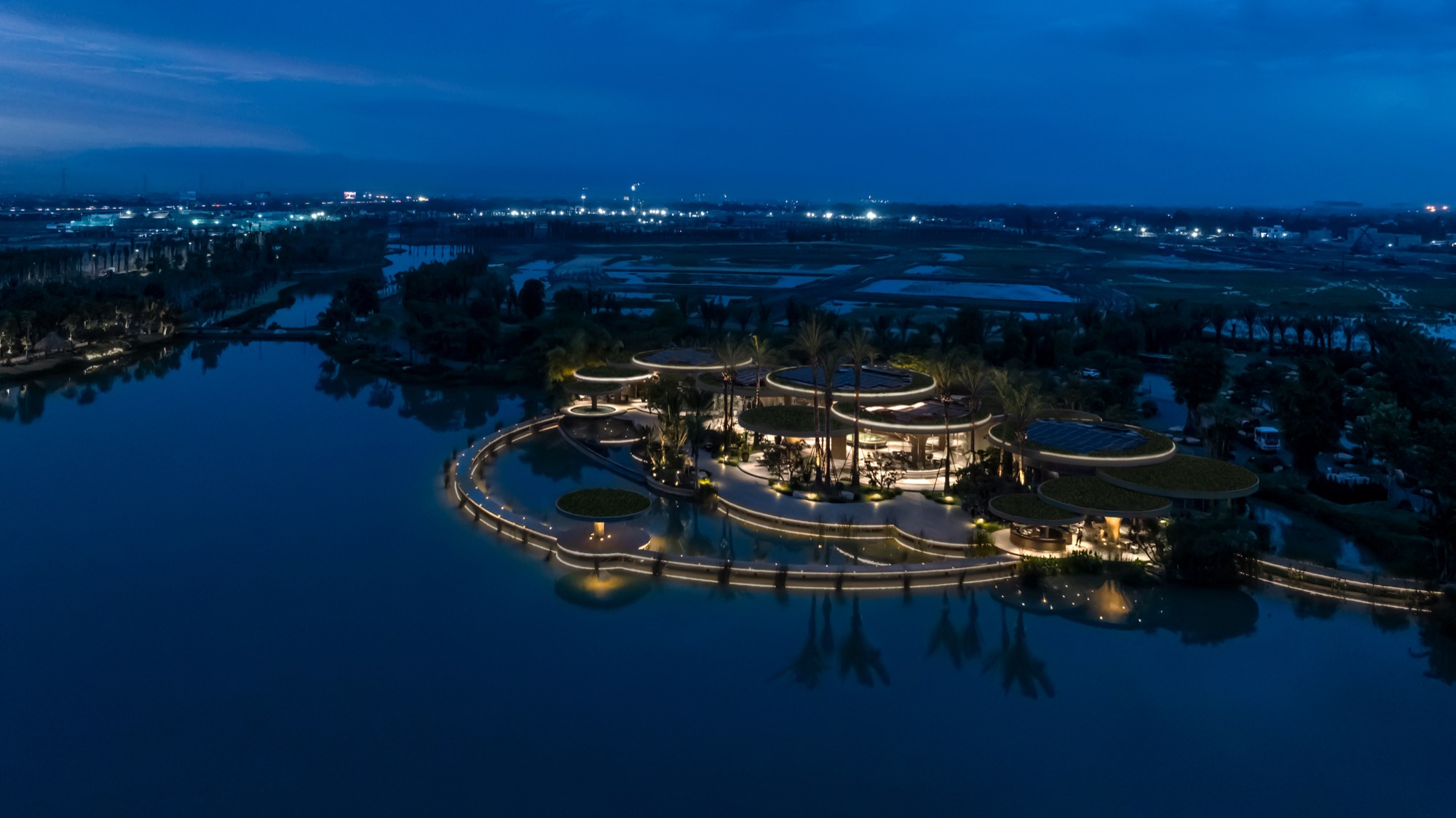 The clubhouse lit at dusk, seen from above across the lake