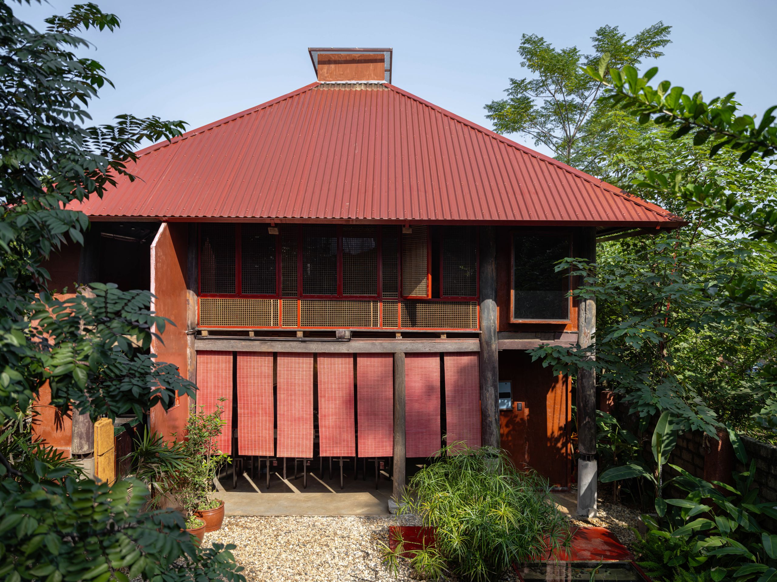 Two-storey timber house under a red corrugated roof